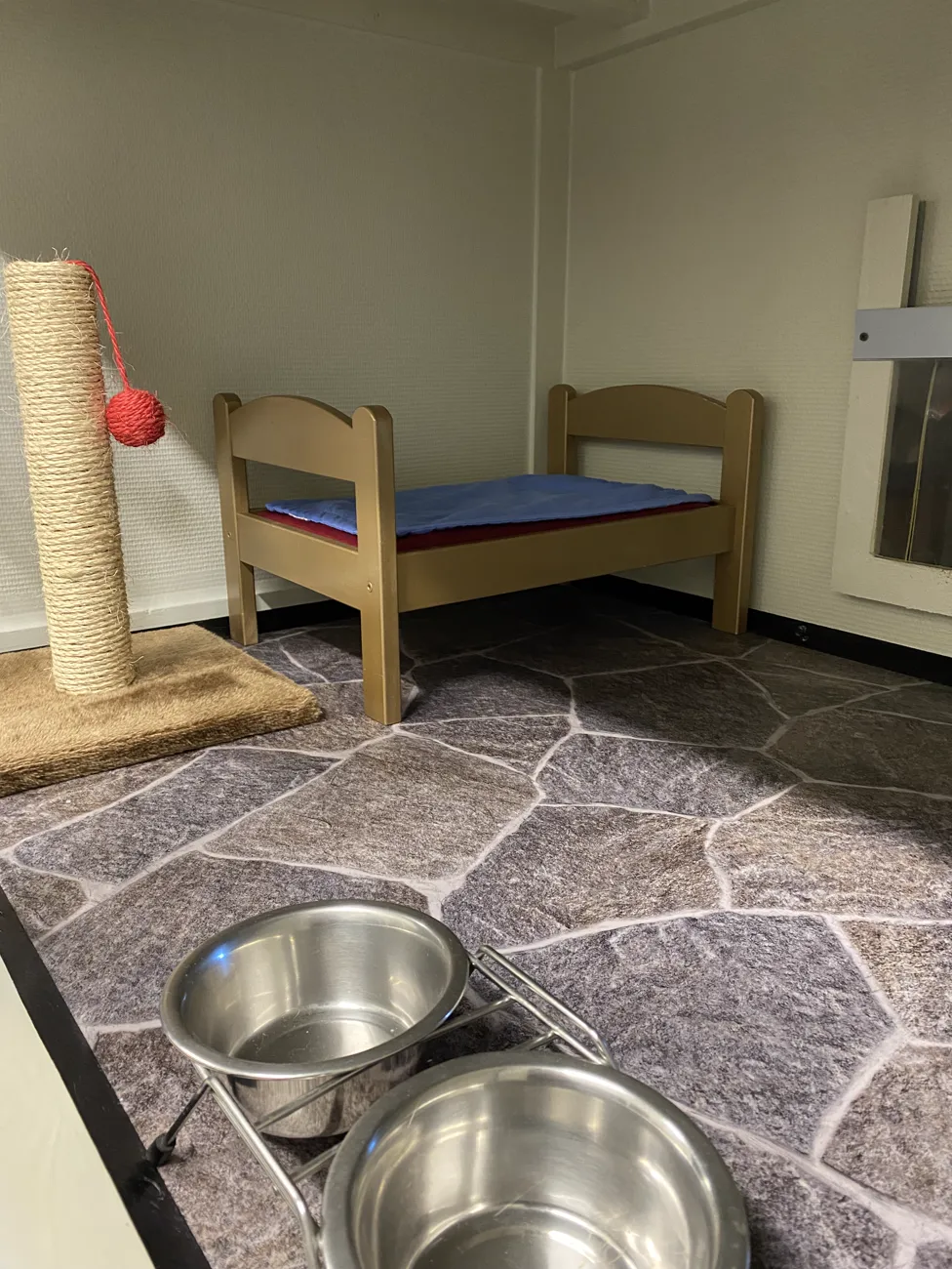 Kattens rom med seng, klorestolpe og vannskåler på steingulv