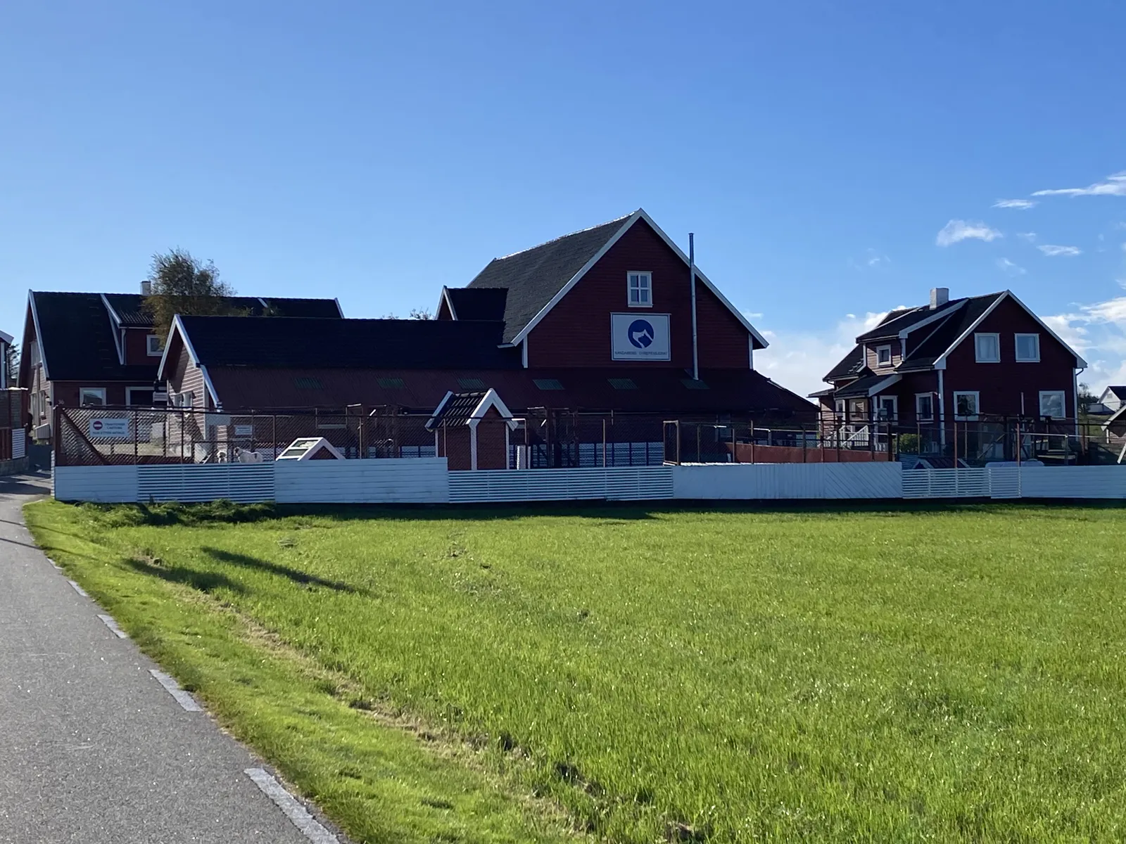 Pensjonatets røde hus og luftegårder sett fra gangveien, med grønn eng i forgrunnen